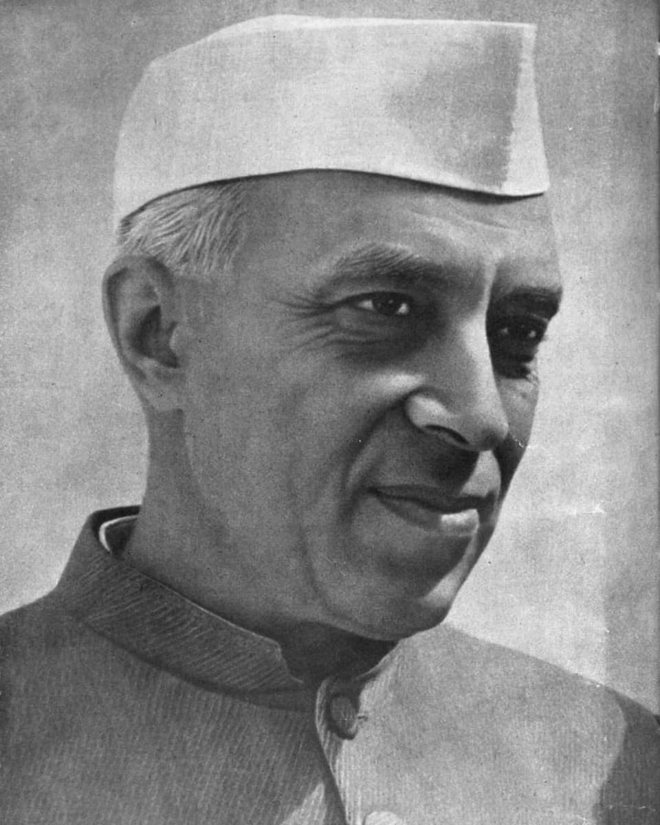 Jawaharlal Nehru in a white cap and buttoned jacket, smiling to one side